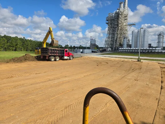 Excavator and dump truck beside a Rocket Engine Test Stand at John C. Stennis Space Center