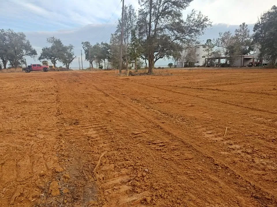 Broad leveled earth surface with retained trees and homes beyond