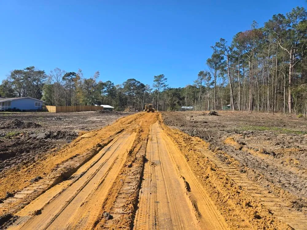 Long earth corridor through a cleared worksite with machine in the distance