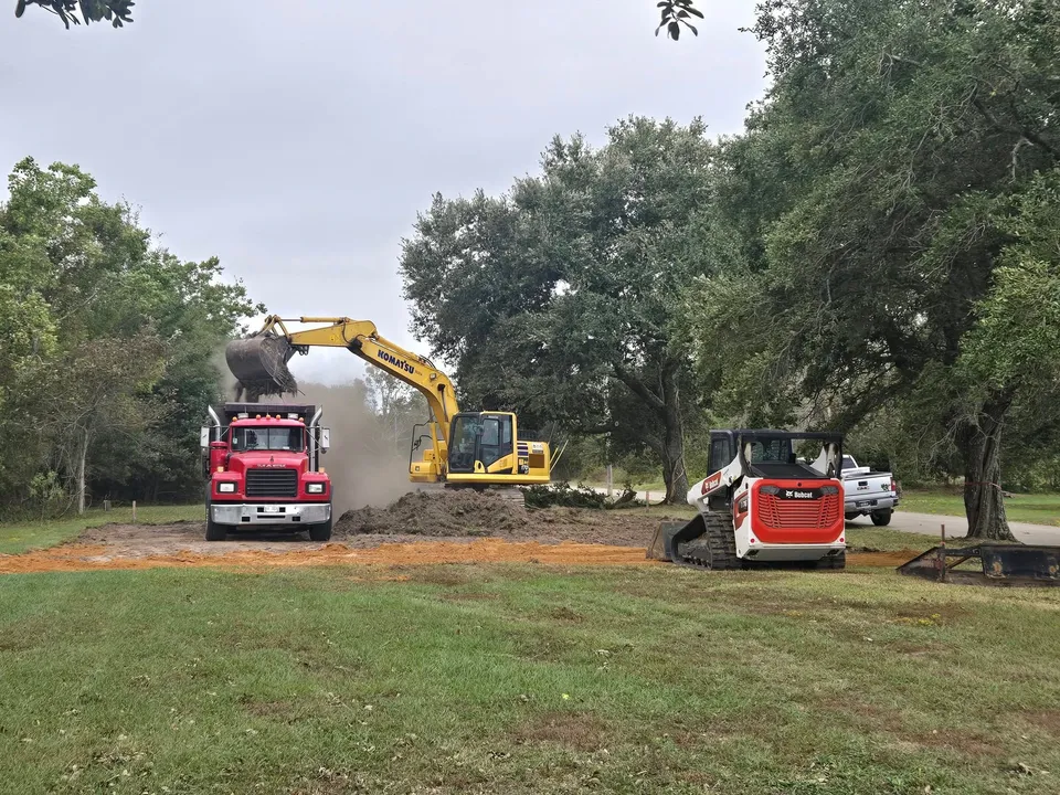 Komatsu excavator loading a red dump truck beside a tracked loader